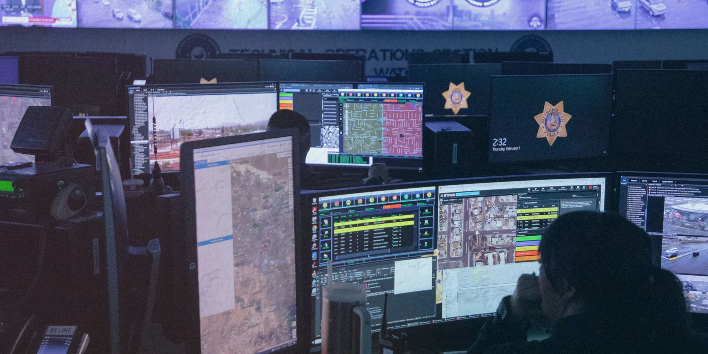 Photo of the Las Vegas Fusion Center, where people in silhouette sit in front of many computer displays, which show maps, live video, and Las Vegas metropolitan police badge logos.
