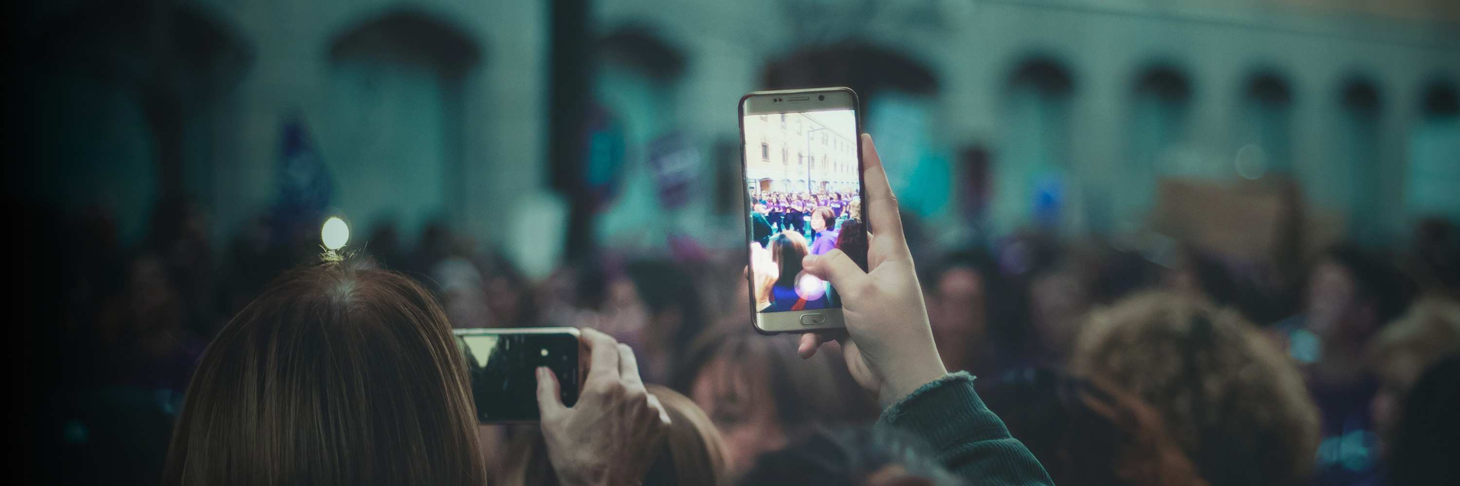 A hand lifts a phone above a crowd to record.